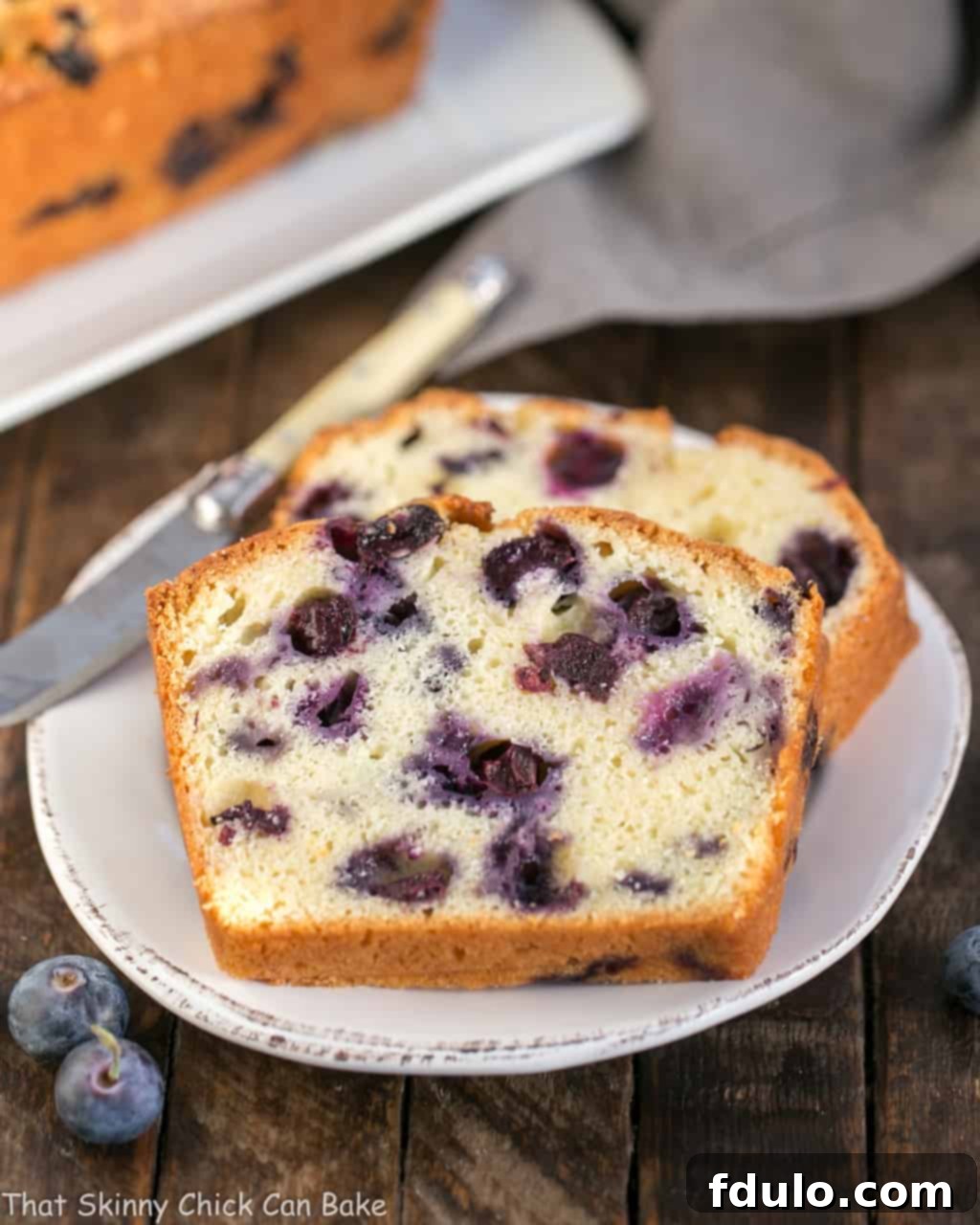 A slice of moist lemon blueberry muffin bread on a white plate, showcasing the berries and tender crumb.