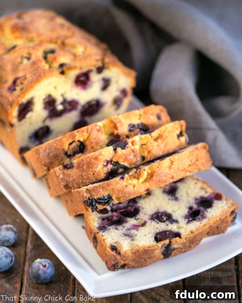 Several slices of golden brown Lemon Blueberry Muffin Bread on a white serving tray, showing the perfectly baked crust and juicy blueberries.