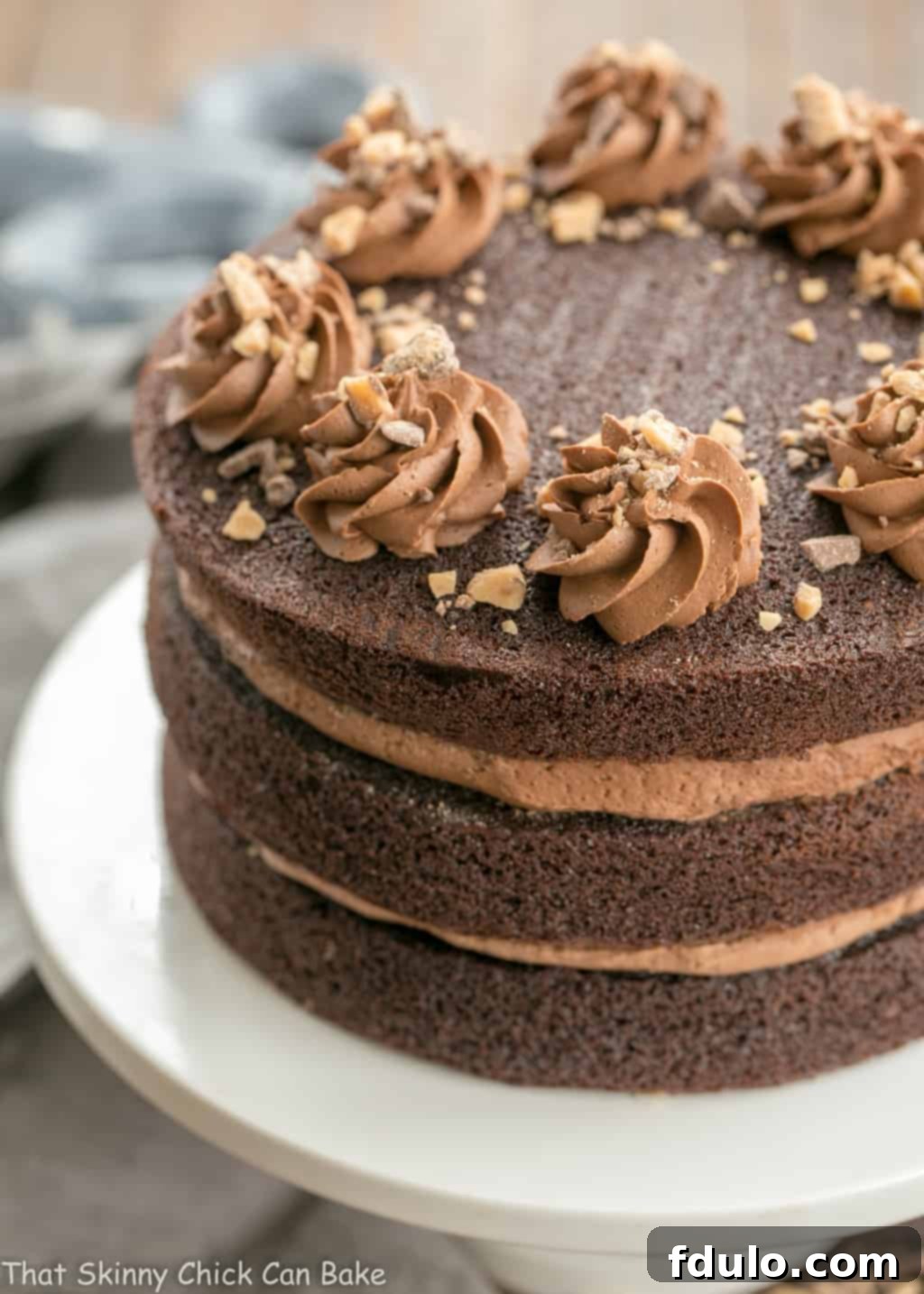 A stunning triple layer chocolate toffee cake on a pristine white cake stand, showcasing its elegant height and frosted perfection.
