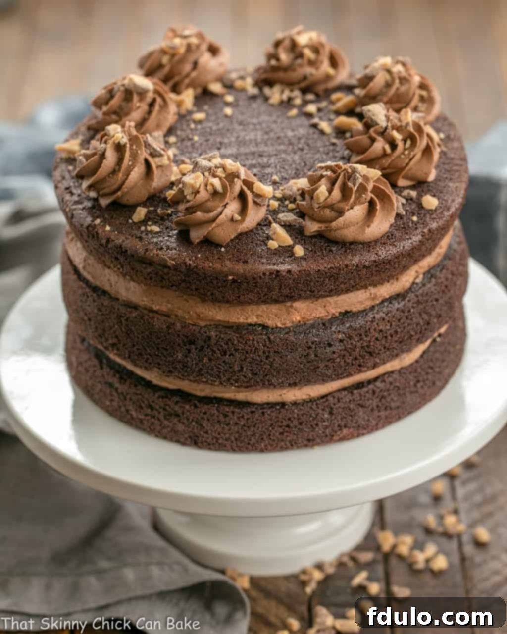 A full side view of the majestic Triple Layer Chocolate Toffee Cake, adorned with elegant frosting swirls, on a delicate white ceramic cake stand.