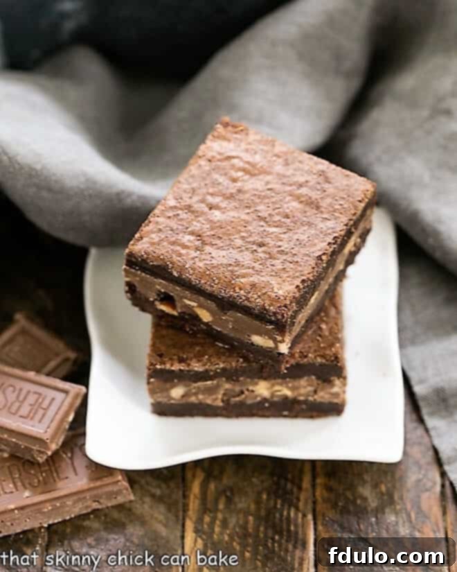 Two rich and fudgy Symphony Toffee Brownies, featuring melted milk chocolate and visible toffee pieces, stacked on a square white dish, ready to be enjoyed.