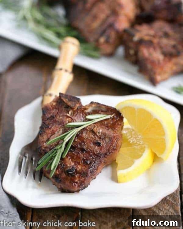 Close-up view of perfectly grilled lamb chops with a golden-brown crust, served on a small white plate alongside a fresh sprig of rosemary and bright lemon wedges, ready to be enjoyed.