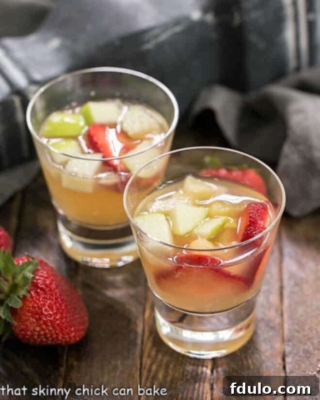 Two elegant glasses of white wine sangria, garnished with fresh strawberries, sitting beside a bowl of extra berries.