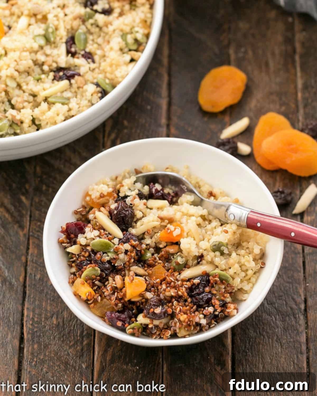 Overhead view of small bowl of quinoa salad with a red handle fork next to serving bowl.