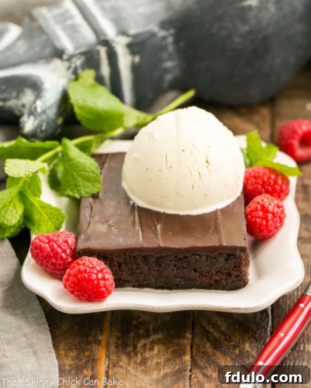 Fudgy Chocolate Sheet Cake with Cocoa Icing - A delectable, ultra-chocolate dessert that feeds a crowd! #sheetcake #chocolate A decadent slice of Fudgy Chocolate Sheet Cake generously topped with a scoop of vanilla ice cream, served on a pristine white dessert plate. The cake's rich, dark chocolate contrasts beautifully with the creamy white ice cream.