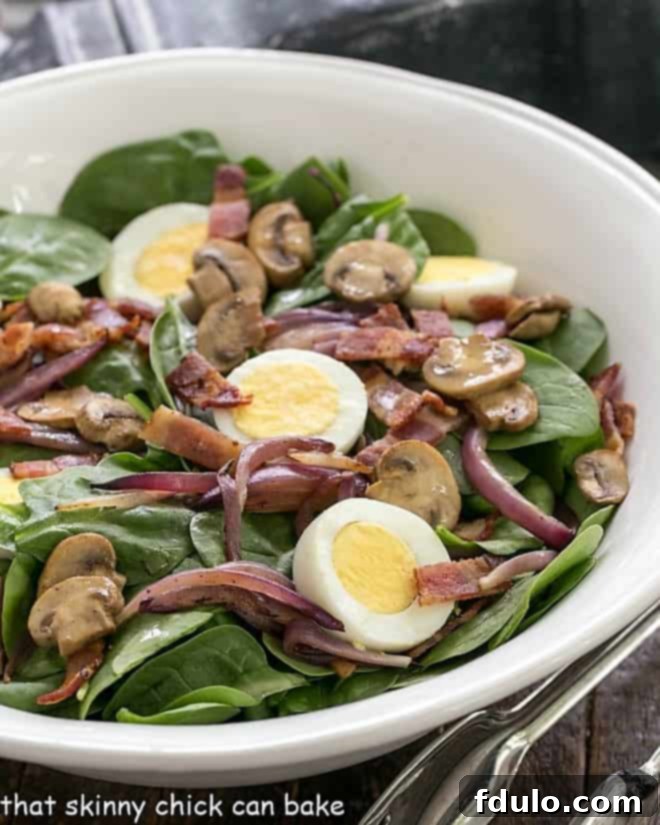 Best Spinach Salad close up in a white ceramic bowl, showcasing vibrant greens, crispy bacon, and perfect eggs.