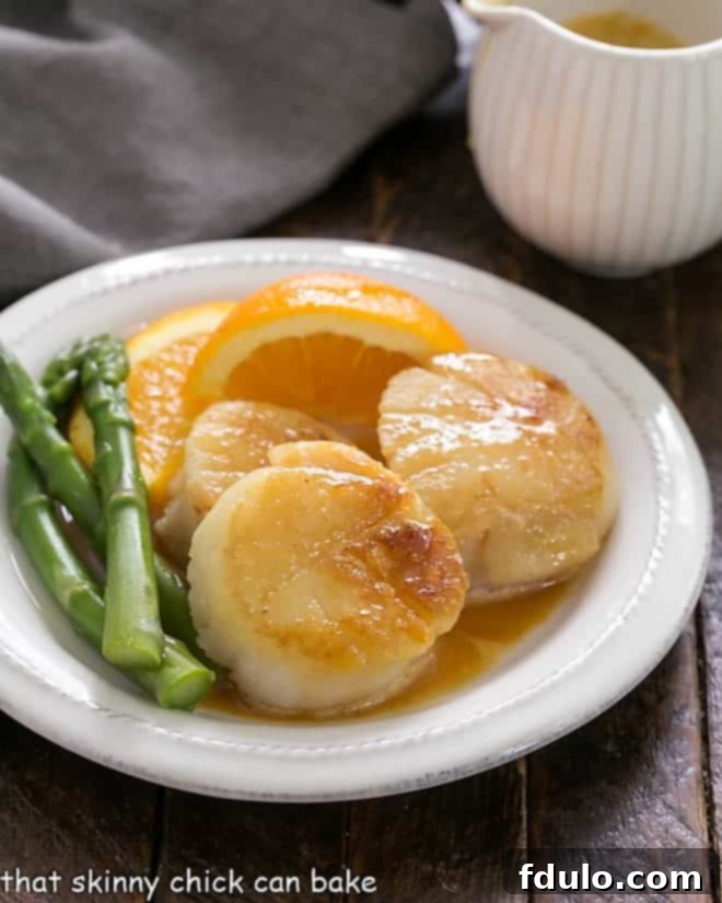Pan Seared Scallops with Caramel Orange Sauce on a white plate with asparagus, elegantly garnished.
