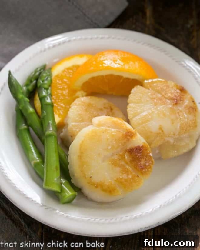 Scallops, asparagus and orange wedge on a white ceramic plate, ready to be enjoyed.