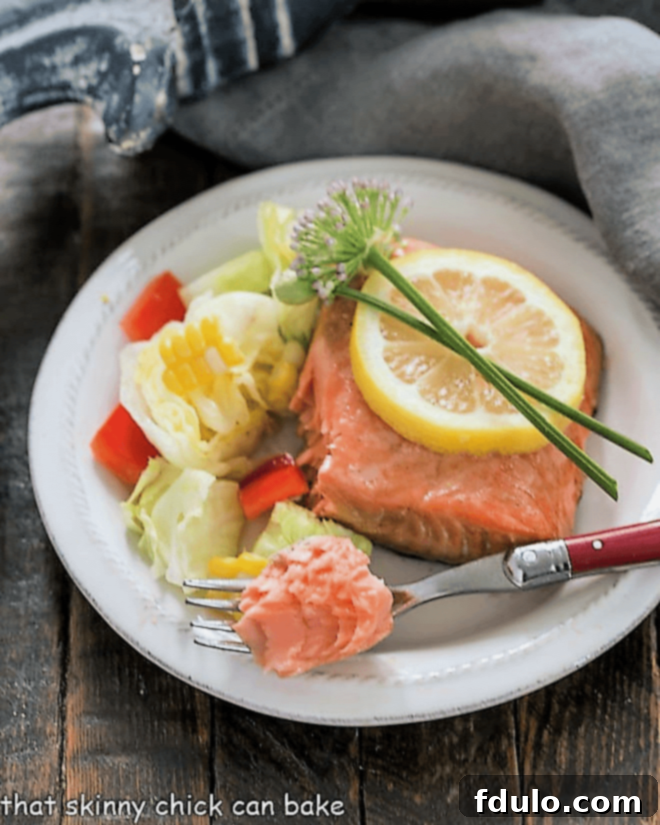 A close-up of a perfectly cooked Easy Glazed Salmon fillet on a white dinner plate, with a fork gently flaking a small, tender piece of salmon.