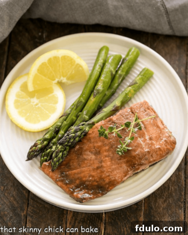 An inviting overhead shot of a glistening salmon fillet, elegantly presented with fresh asparagus and vibrant lemon wedges, suggesting a healthy and delicious meal.
