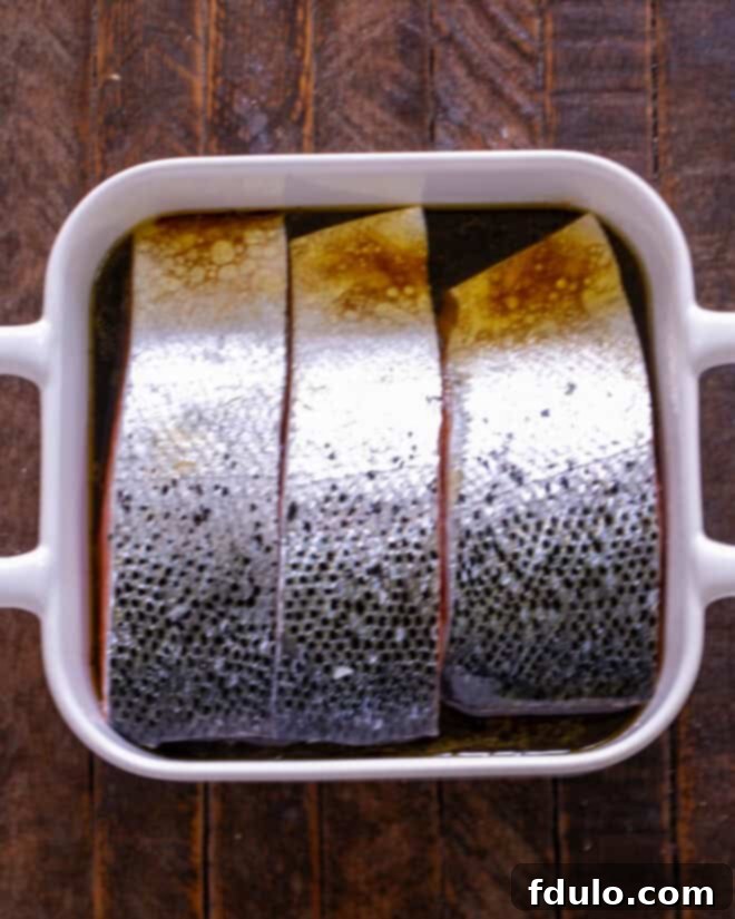 Salmon fillets placed flesh-side down in the marinade in a baking dish, ensuring maximum flavor absorption.
