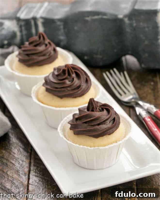 Three perfectly crafted Boston Cream Pie Cupcakes presented on an elegant white tray, accompanied by two charming red-handled forks, ready to be enjoyed.