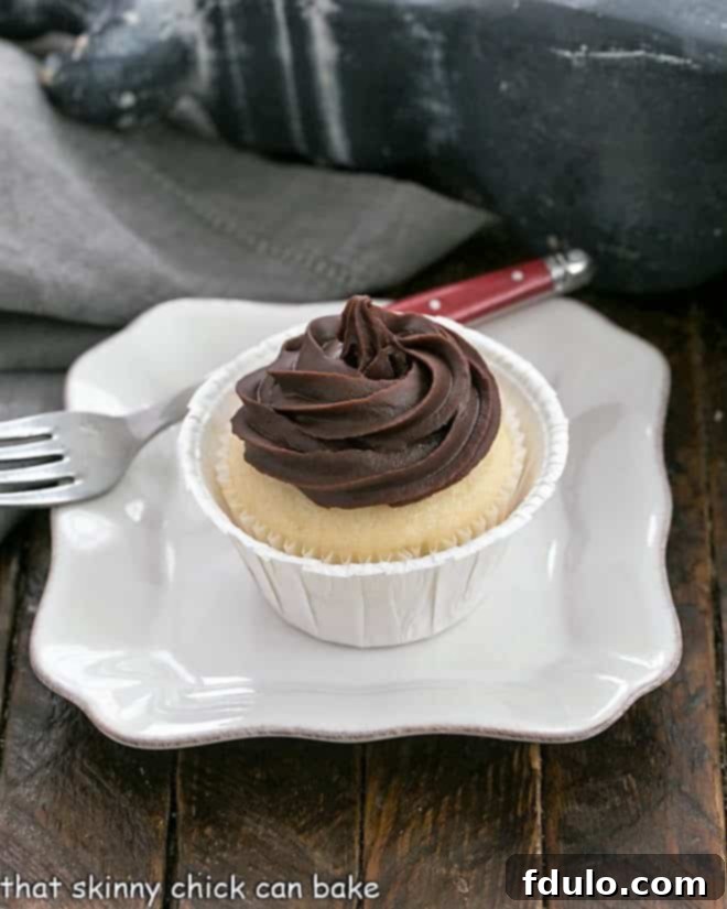 A single, perfectly adorned Boston Cream Pie Cupcake resting on a pristine white plate, showcasing its golden cake, creamy filling, and elegant chocolate ganache swirl.