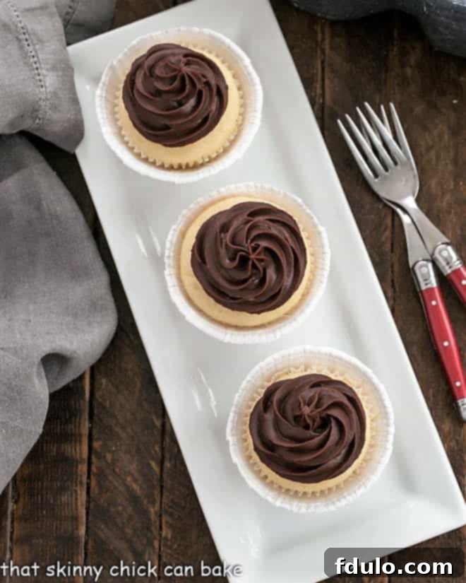 An inviting overhead view of three beautifully presented Boston Cream Pie Cupcakes arranged on a sleek, narrow white platter, adorned with generous swirls of chocolate ganache.