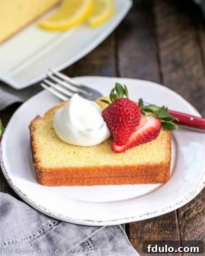 A beautifully plated slice of Glazed Lemon Pound Cake with fresh berries and whipped cream, showcasing its moist texture and golden glaze.