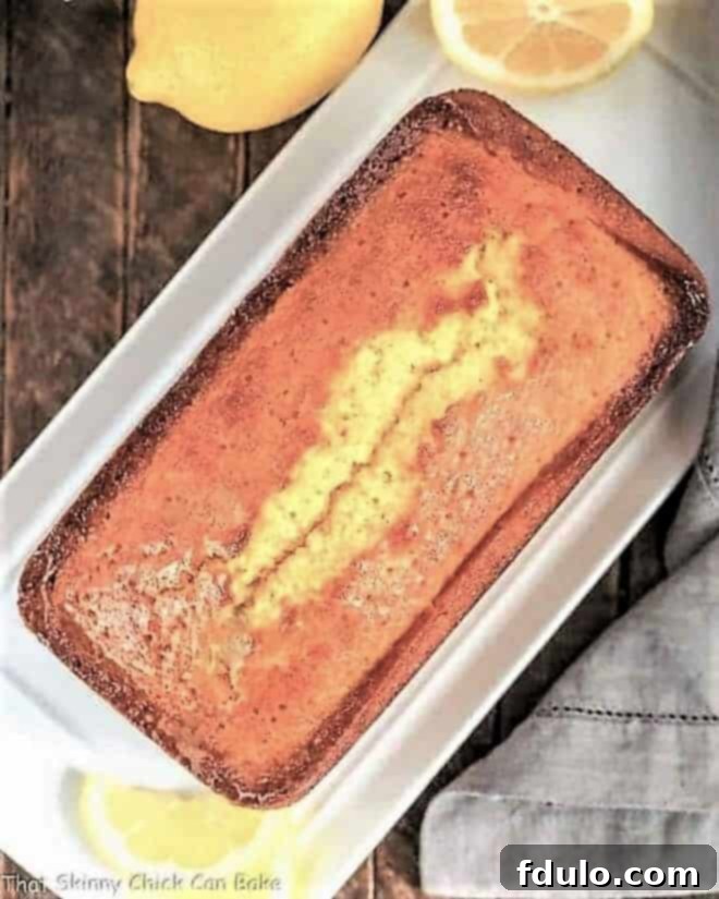 Overhead view of a Glazed Lemon Pound Cake loaf on a white serving tray, showcasing its golden-brown crust and glistening lemon glaze.