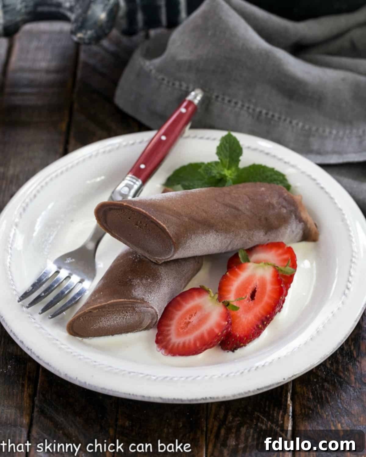 Frozen Chocolate Crepes filled with a rich chocolate mousse and served over creme anglaise. These elegant French pancakes are made in the blender for easy pouring! Frozen chocolate crepe sliced in half and served over creme Anglaise with sliced strawberries, ready to be enjoyed as an elegant dessert.