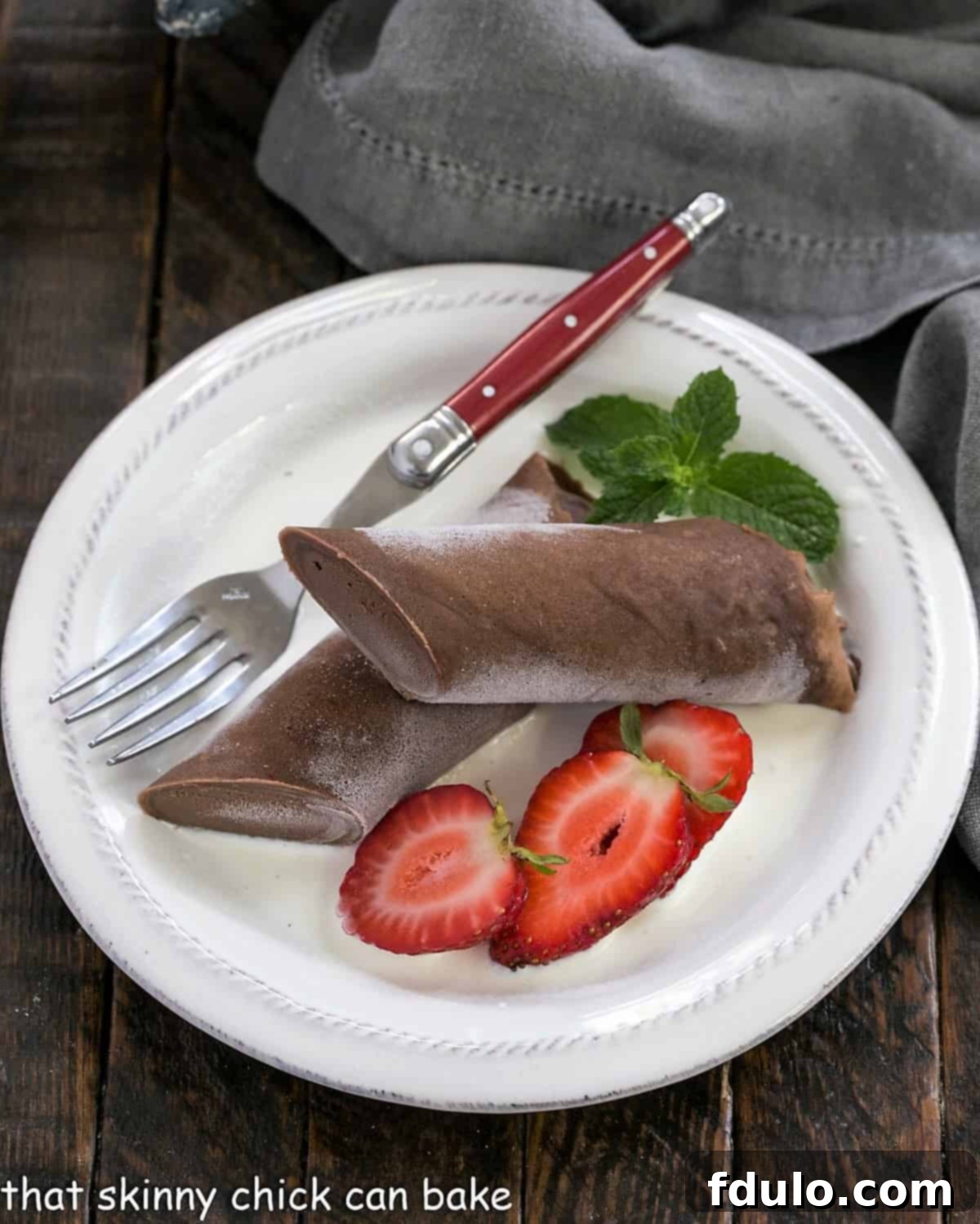 Icy Chocolate Crêpe Bliss 3 Overhead view of a beautifully presented frozen chocolate crepe with fresh berries on a white plate, accompanied by a stylish red-handled fork, ready for a delightful dessert experience.