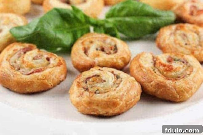 Flaky Prosciutto Gruyère Pinwheels, perfect for parties Golden brown Prosciutto Gruyère Pinwheels on a white serving platter, garnished with fresh basil