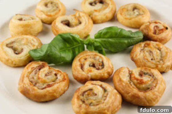 Elegant Prosciutto Gruyère Pinwheels, ready to serve Baked Prosciutto Gruyère Pinwheels artfully arranged on a white tray with a sprig of fresh basil
