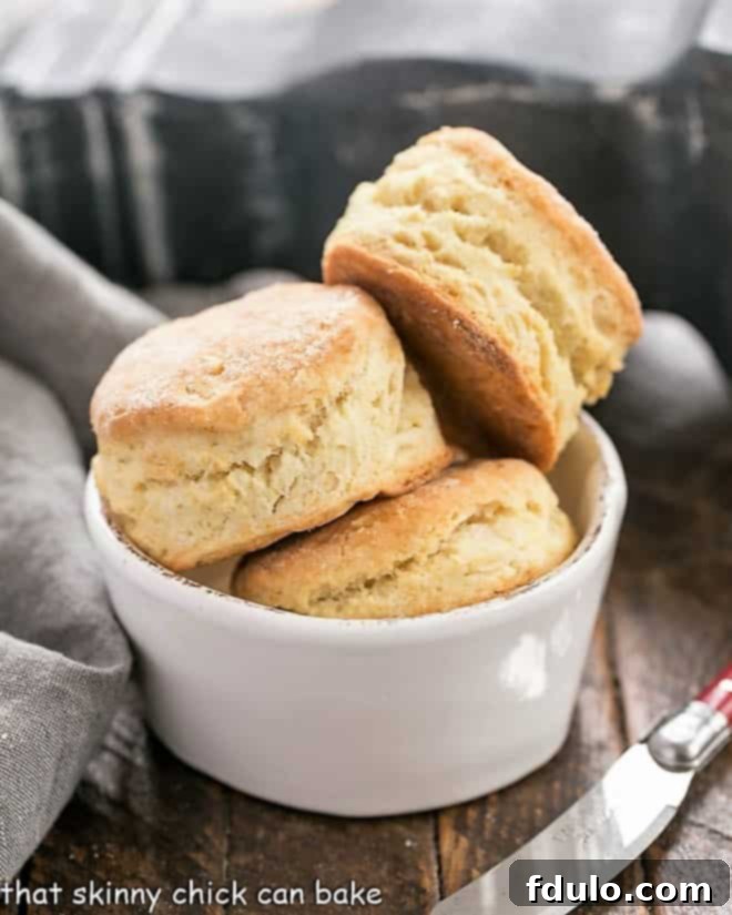 A charming white ceramic bowl overflowing with freshly baked homemade buttermilk biscuits, their golden-brown tops hinting at the flaky layers within.