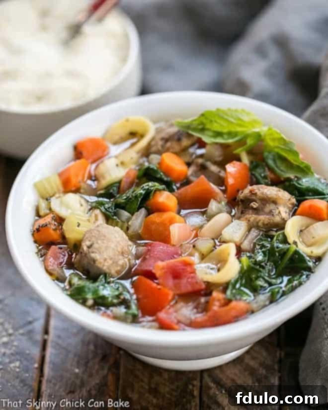 A beautiful close-up of Italian Sausage and Pasta Soup in a white soup bowl, with a small bowl of grated Parmesan cheese beside it, ready for serving.