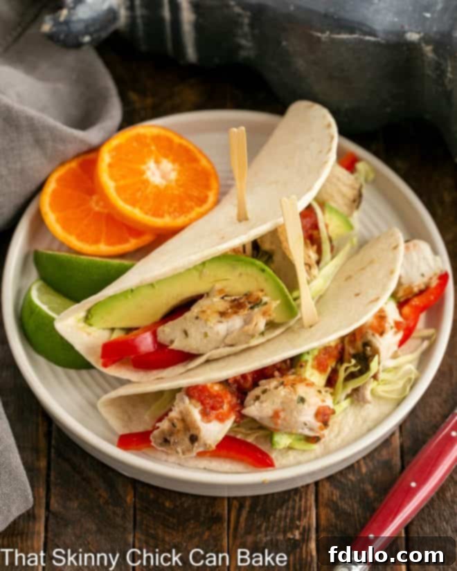 Two perfectly grilled fish tacos, generously filled with flaky fish and crisp slaw, served on a pristine white plate.