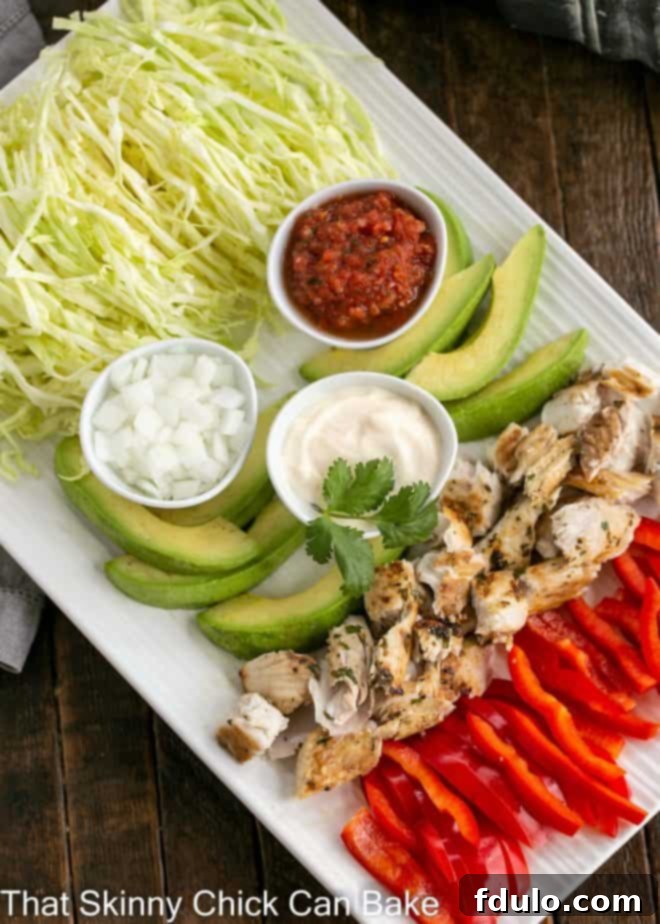 Overhead shot of an assembled fish taco platter featuring grilled fish, shredded cabbage, sliced avocado, fresh cilantro, lime wedges, and a creamy sauce on a white ceramic platter.