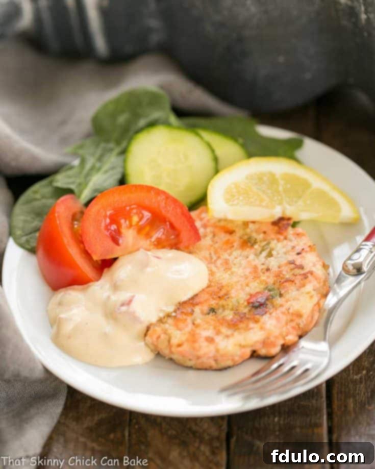 A white plate with a salmon cake, salad and remoulade sauce
