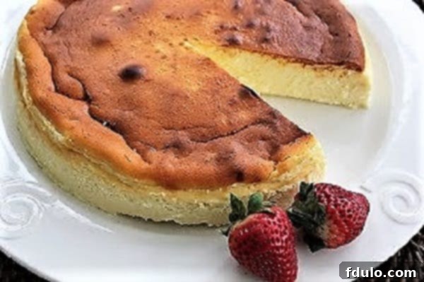 A beautifully baked Ricotta Cheesecake, golden brown on top, resting on a white cake plate with a single slice removed, revealing its creamy interior.