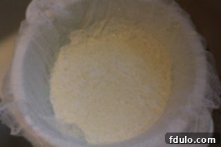 Homemade ricotta draining in a cheesecloth-lined colander, with clear whey dripping away, showcasing the process