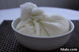 Freshly drained ricotta wrapped in cheesecloth, compact and ready for use in the cheesecake recipe