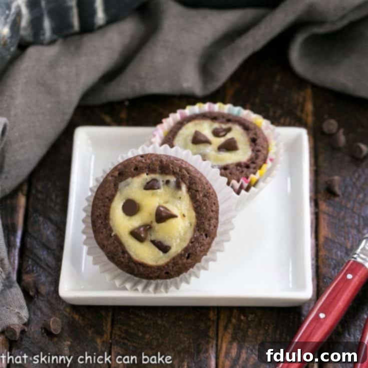 Two mini chocoate cupcakes on a square white plate, with one partially eaten, revealing the creamy center.