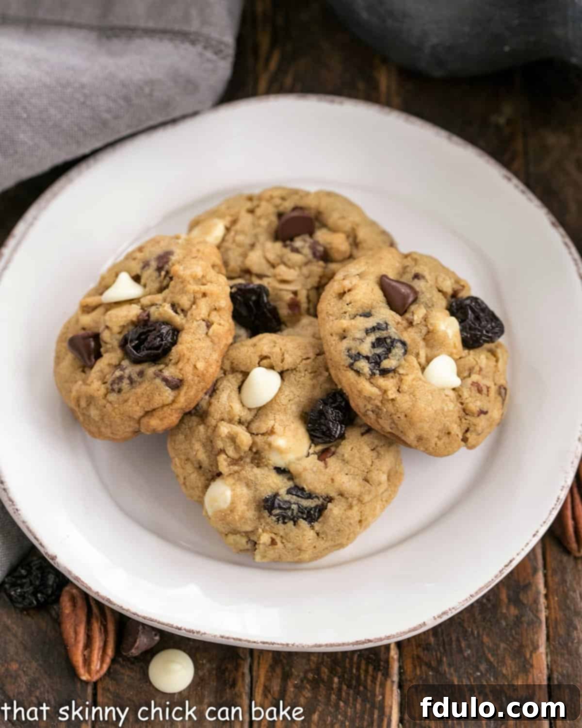 Overhead view of several golden-brown Chewy Oatmeal Cookies arranged on a white plate, highlighting their various textures from the oats, chocolate, pecans, and dried cherries.