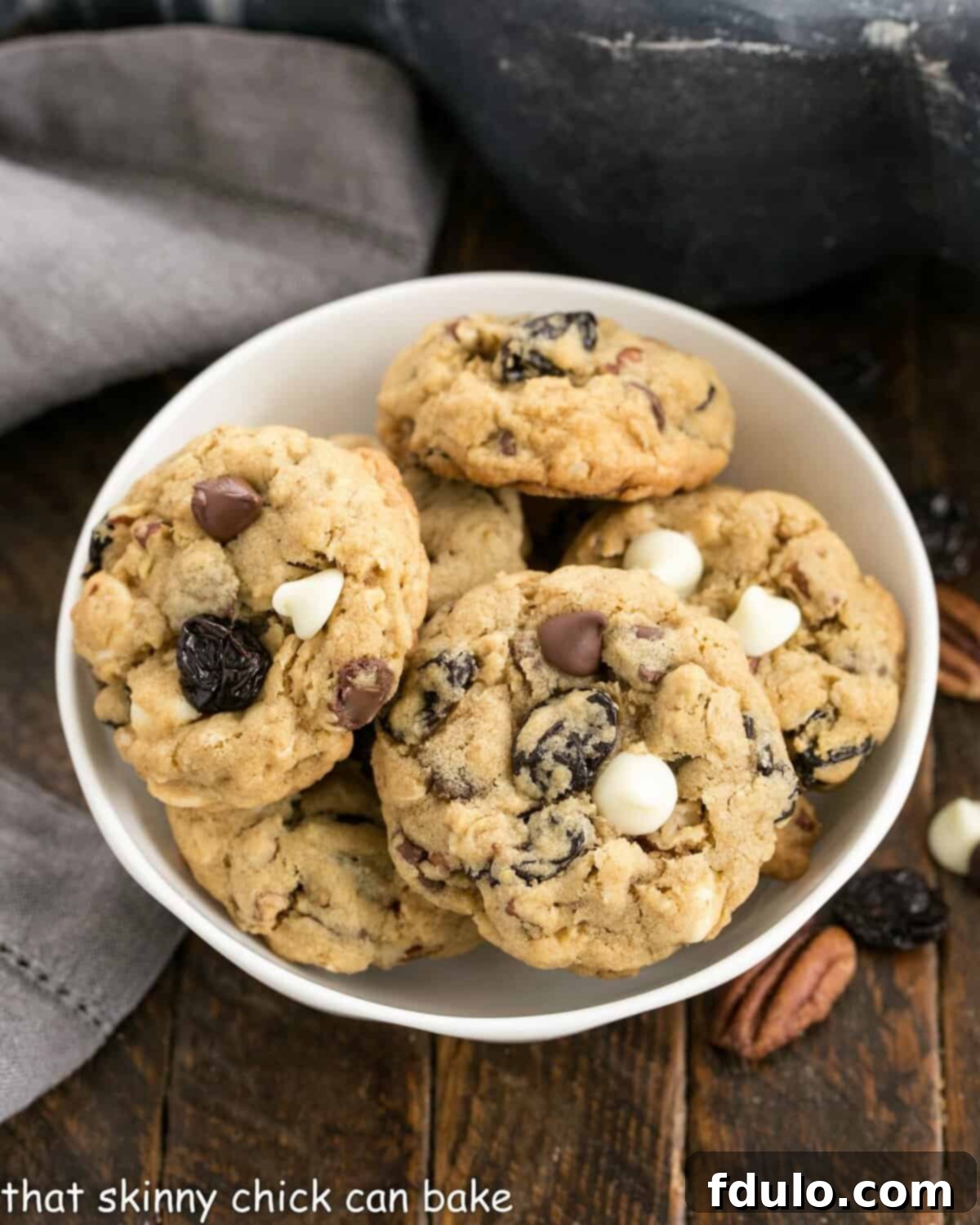 Overhead view of a beautiful bowl overflowing with Chewy Oatmeal Cookies, rich with chocolate, pecans, and dried cherries, ready to be enjoyed.