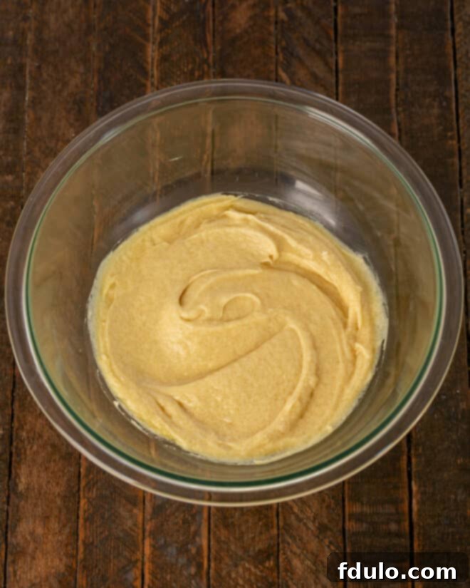 Step 1: Mixing cooled melted butter with both granulated and brown sugars, followed by vanilla extract and a single egg until creamy.