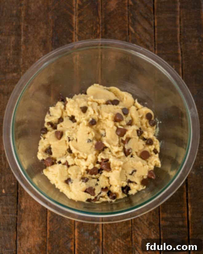 Step 3: Folding in a generous amount of semisweet and milk chocolate chips into the prepared cookie dough, then covering the bowl for a crucial chilling period in the refrigerator.