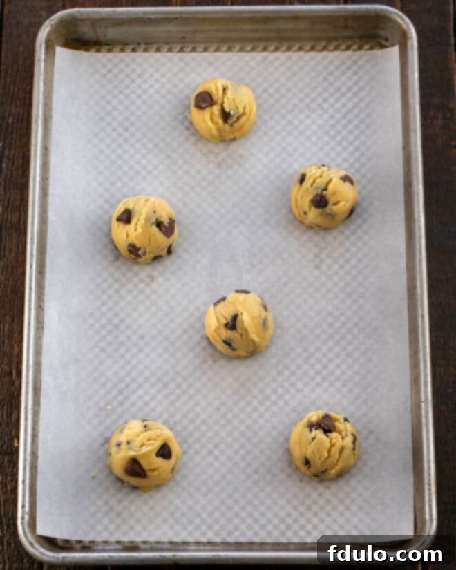 Step 4: Using a cookie scoop to portion uniform balls of chilled cookie dough onto a parchment-lined baking sheet, ensuring adequate spacing between each for optimal baking and spreading.