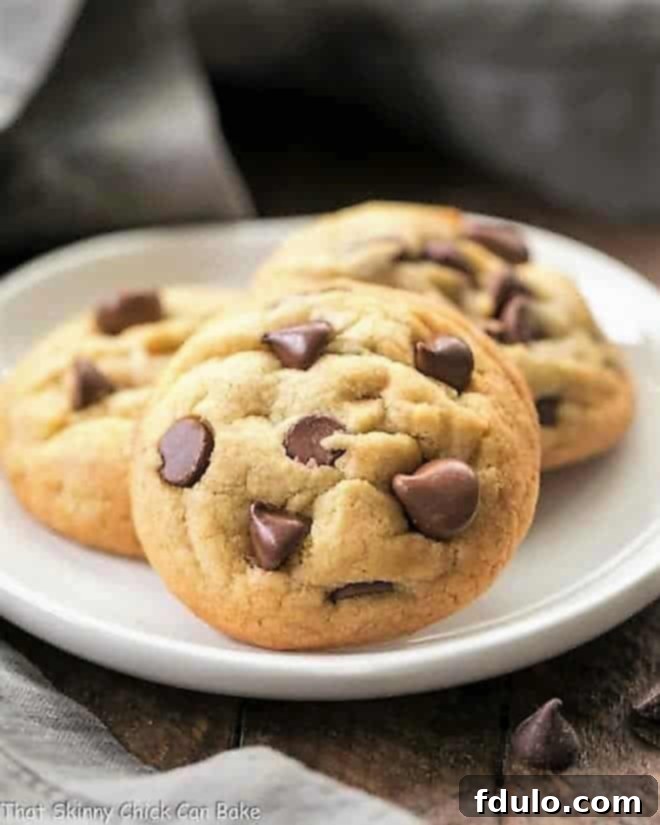 A perfectly baked Double Chocolate Chip Cookie, generously studded with melted chocolate chips, presented on a small, elegant white plate, ready to be savored.