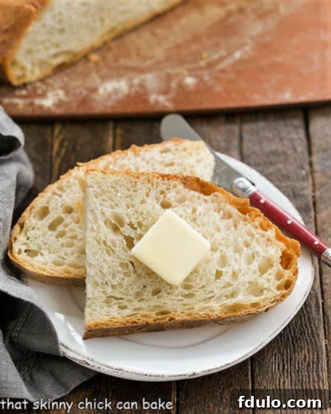 Slices of this Easy Bread Recipe with a pat of butter on a small white plate, showcasing the rustic crust and open crumb.