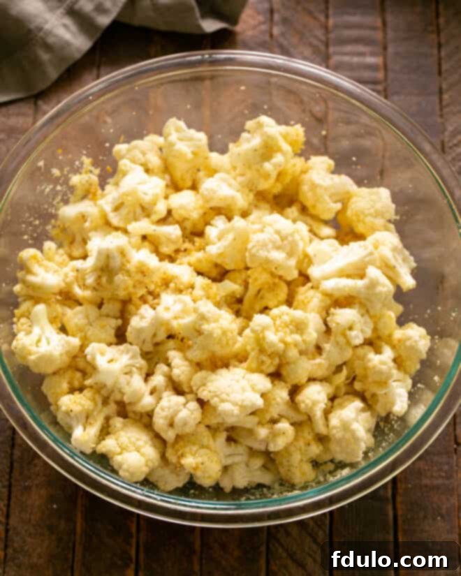 Bowl of cauliflower florets freshly tossed with olive oil and grated Parmesan cheese, glistening and ready for the next step.