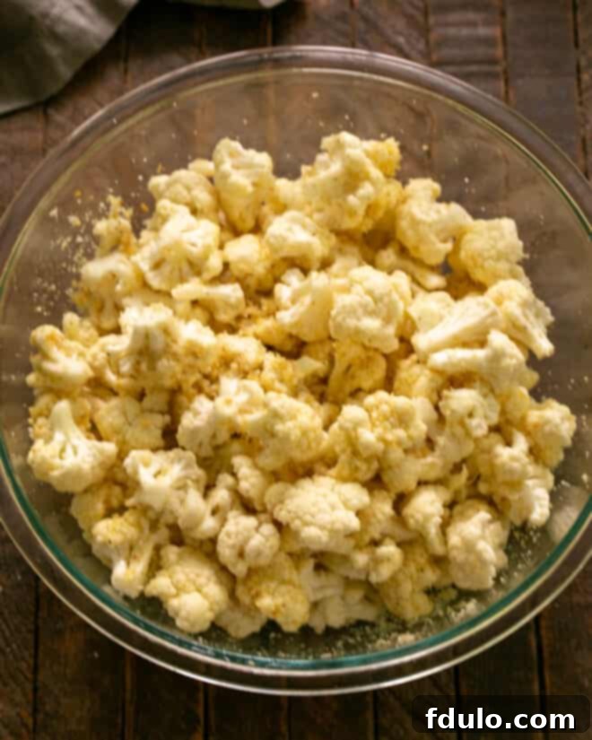 Bowl of cauliflower florets now coated with bread crumbs and additional Parmesan, showing an even distribution of the crispy topping.