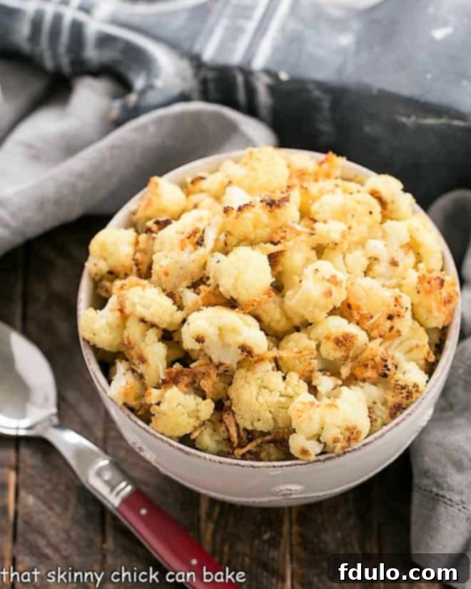 Overhead view of a round white bowl filled with perfectly roasted cauliflower florets, golden-brown and garnished with a sprinkle of fresh Parmesan and breadcrumbs, ready for serving.