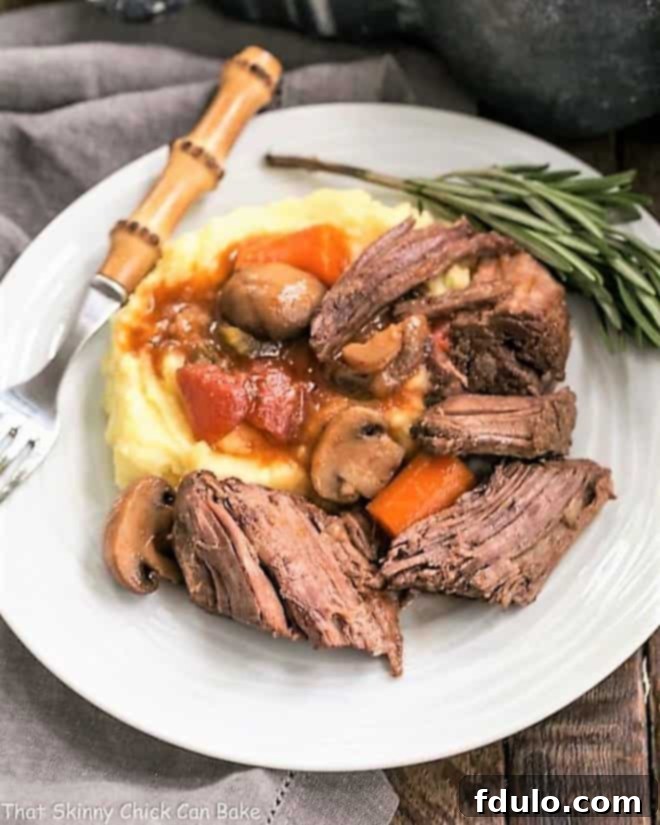 Oven Pot Roast Recipe with Mushrooms, Tomatoes & Red Wine - marvelous comfort food with an exquisite depth of flavor! Pot Roast with Mushrooms, Tomatoes & Red Wine on a white plate with mashed potatoes and a sprig of rosemary.