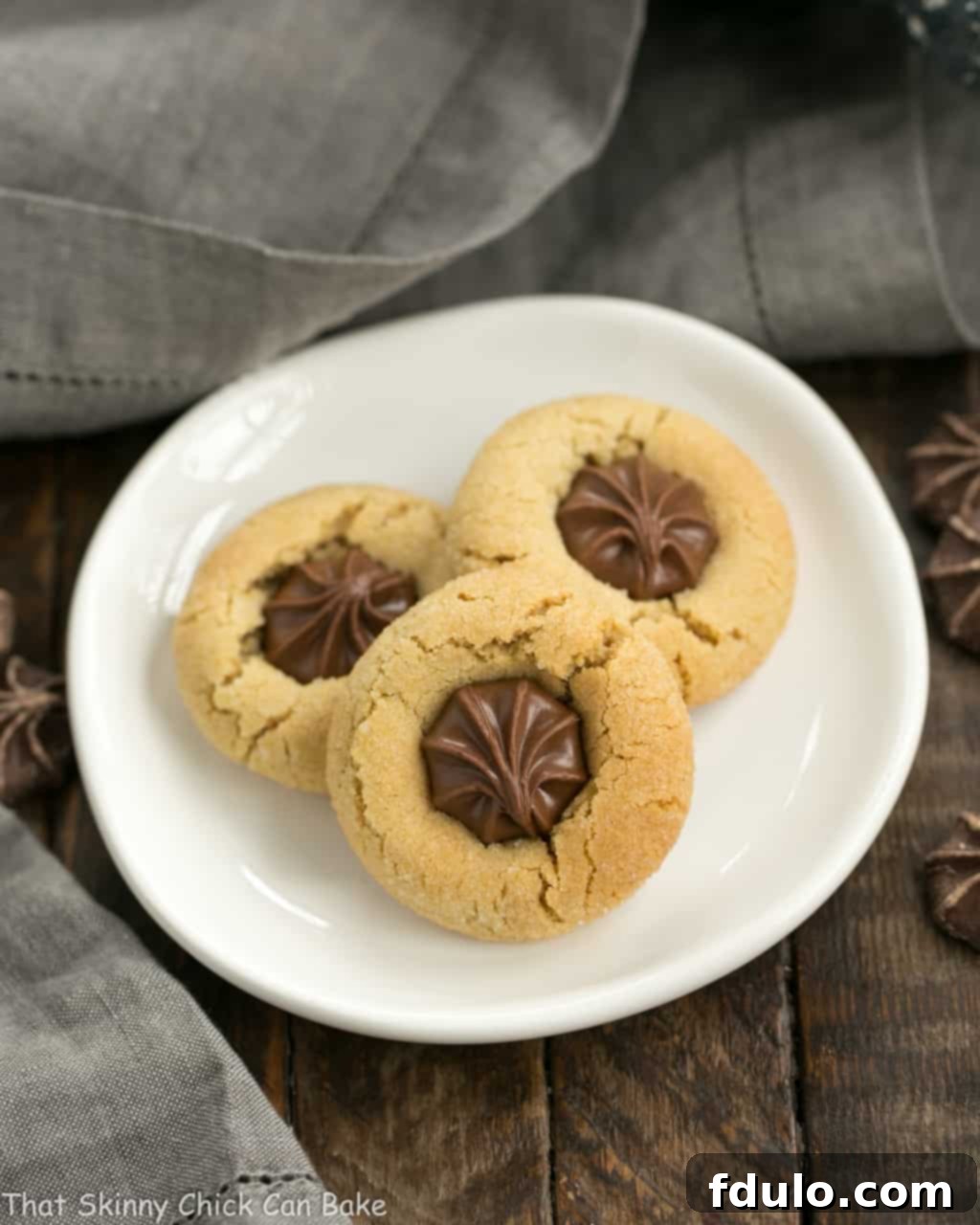 An appetizing close-up of Peanut Butter Blossoms, or Star of Bethlehem Cookies, arranged artfully on a small white plate, showcasing their perfect shape and chocolate star topping.