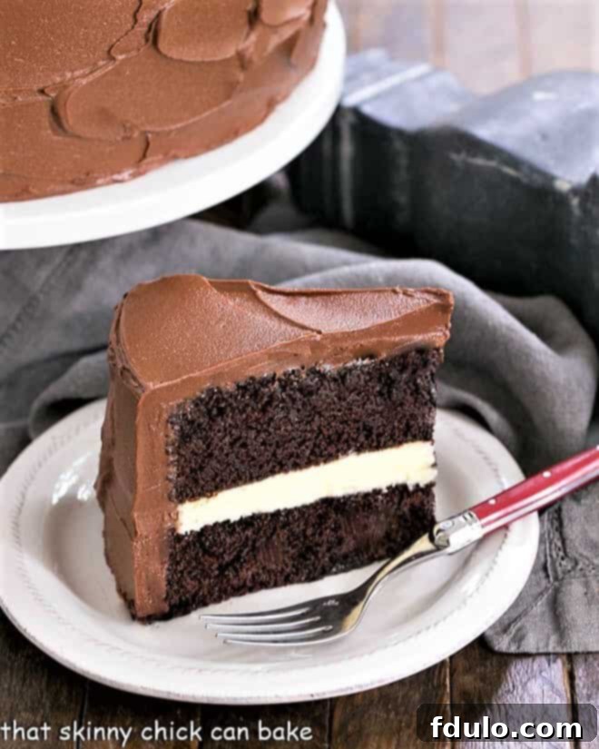 Slice of Chocolate Layer Cake with White Chocolate Ganache on a white dessert plate with a red handled fork, showing the creamy filling.