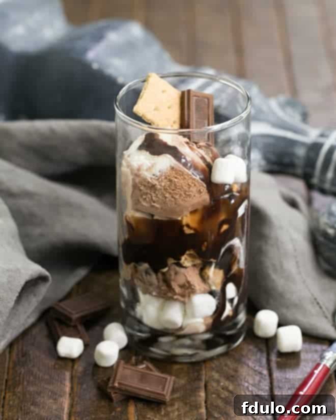 Close-up of a S'mores Ice Cream Sundae overflowing with ice cream, fudge sauce, mini marshmallows, and graham cracker pieces, ready to be enjoyed as a frozen summer treat.