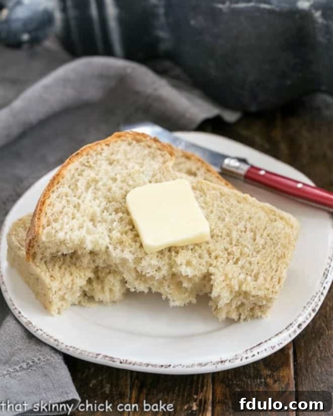 Oatl Bread - a sweet, hearty yeast bread recipe flavored with a touch of brown sugar A slice of freshly baked oatmeal bread, gently torn in half, revealing its soft, tender interior. It's served on a pristine round white plate, accompanied by a small pat of butter and a red-handled butter knife.