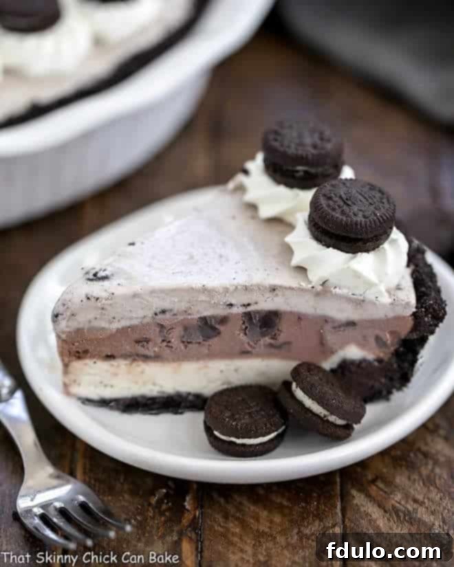 A perfectly sliced piece of Layered Ice Cream Pie with Chocolate Cookie Crust on a white plate, revealing distinct layers.