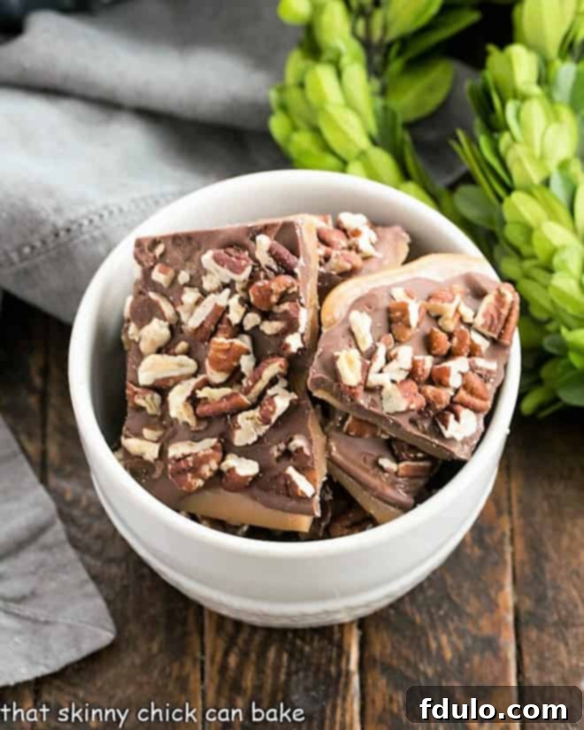 Overhead view of a white bowl filled with Christmas toffee pieces, some topped with chocolate and pecans.